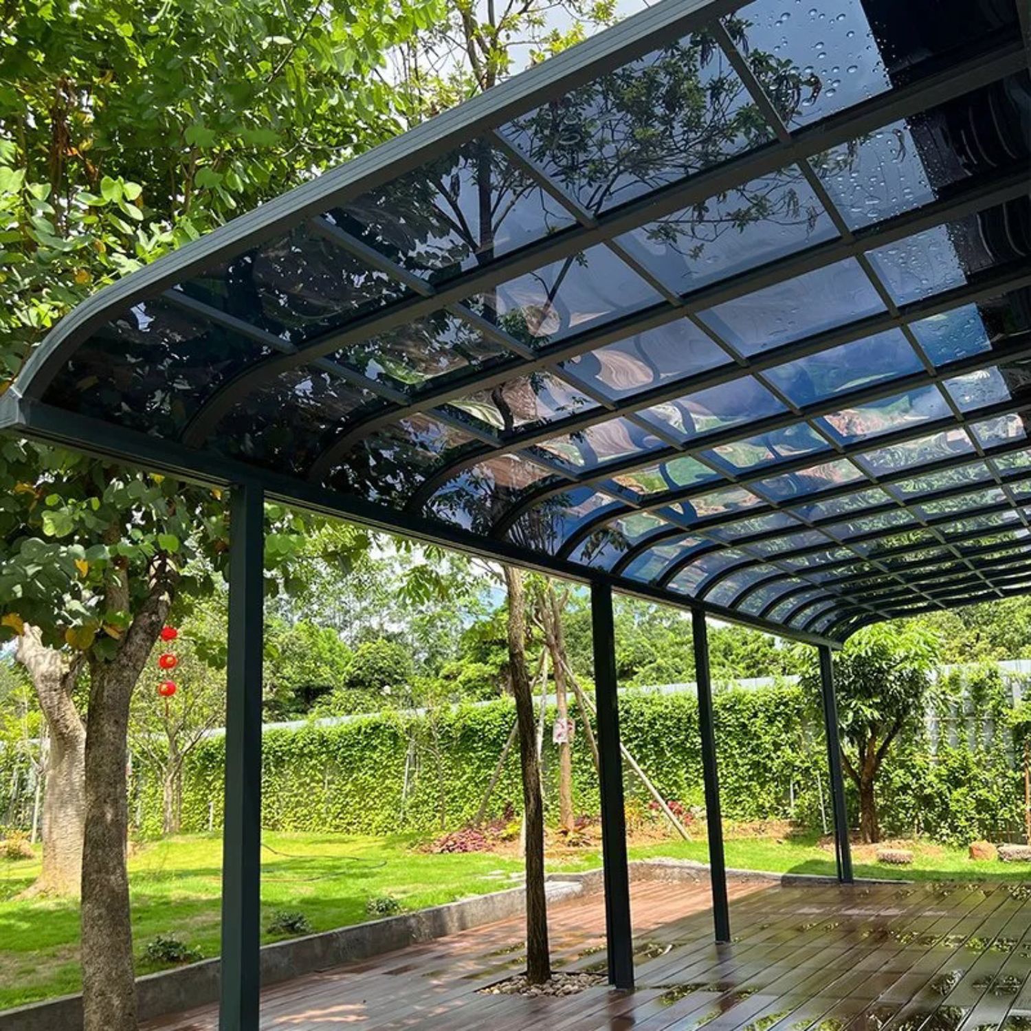 Mái che sân bằng tấm lợp polycarbonate khung sắt đen hiện đại trong khuôn viên cây xanh.